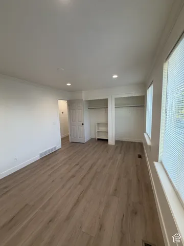Wood-finish flooring, recessed ceiling lighting, built-in shelving, and two windows with blinds