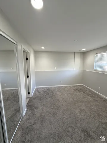 Recessed lighting, neutral paint palette, window with blinds, gray carpeting, and mirrored sliding closet doors