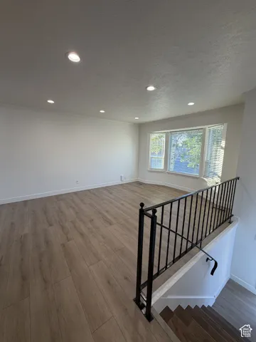 Spacious living area featuring recessed lighting, wood-finish flooring, a bay window, and a wrought iron railing
