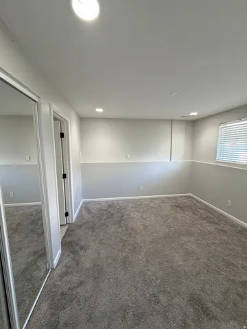 Recessed lighting, neutral paint palette, window with blinds, gray carpeting, and mirrored sliding closet doors