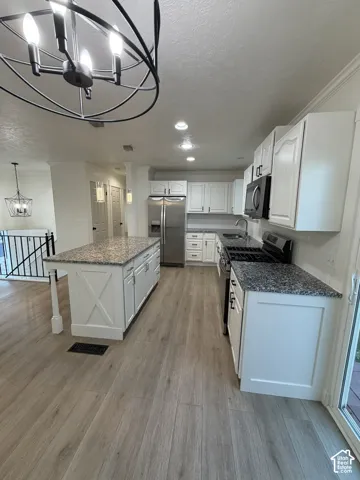 Kitchen featuring white cabinetry, stone-finish countertops, a central island with X-detailing, stainless steel appliances, and wood-finish flooring