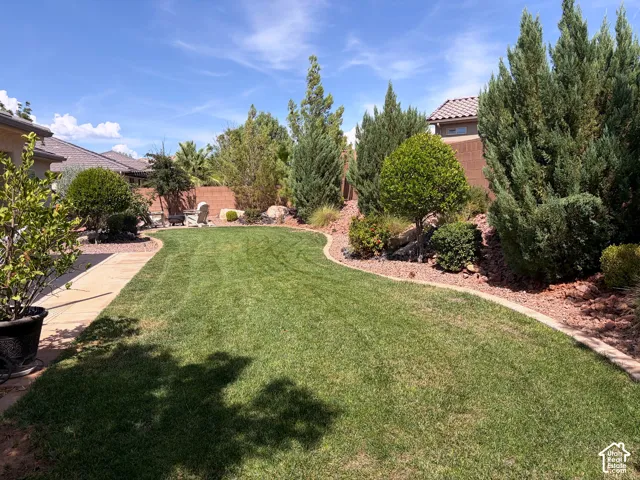 Expansive backyard featuring a manicured lawn, established landscaping, and a paver pathway