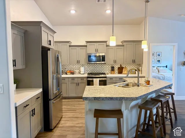 Kitchen with stainless steel appliances, light gray cabinetry, a tile backsplash, and a granite island with a built-in sink