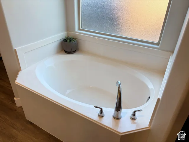 Corner soaking tub with chrome fixtures, a surrounding white countertop, and a privacy window