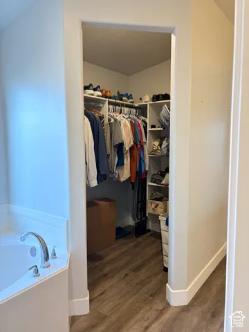 Corner soaking tub with chrome fixtures and a separate walk-in closet featuring wood-finish flooring