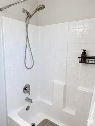 Bathtub with integrated shower, white tile surround, and chrome fixtures