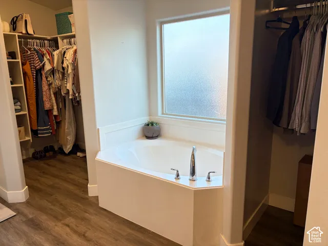 Built-in corner soaking tub with deck-mounted fixtures, privacy window, and wood-finish flooring