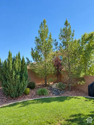 Expansive backyard featuring a manicured lawn, established landscaping, and a block fence