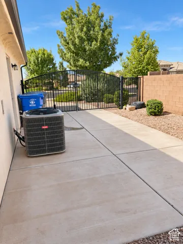 Paved concrete pathway with a wrought iron fence and gate, a block wall, and gravel landscaping