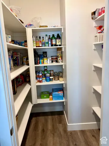 Spacious pantry with multiple built-in white shelves, wood-finish flooring, and white trim