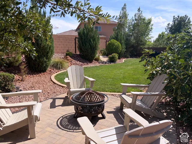 Paver patio with a central fire pit, surrounded by a manicured lawn, gravel landscaping, and mature trees