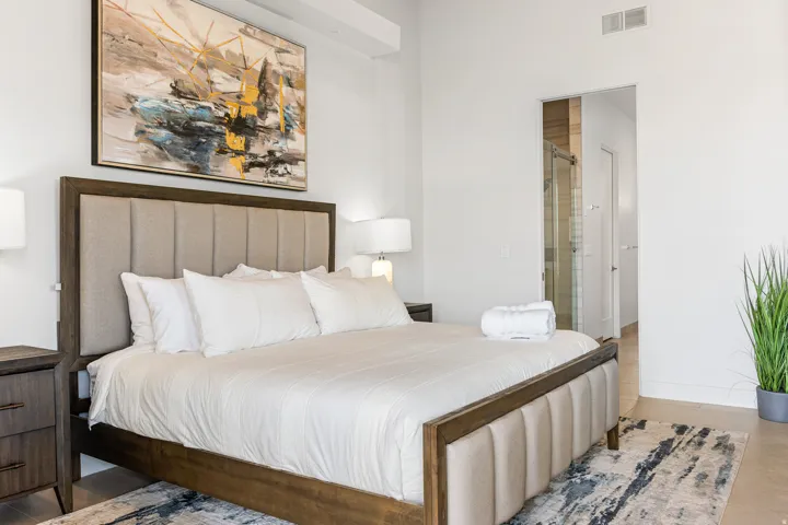 Expansive bedroom featuring high ceilings, wood-finish flooring, a contemporary bed frame with an upholstered headboard, and recessed lighting
