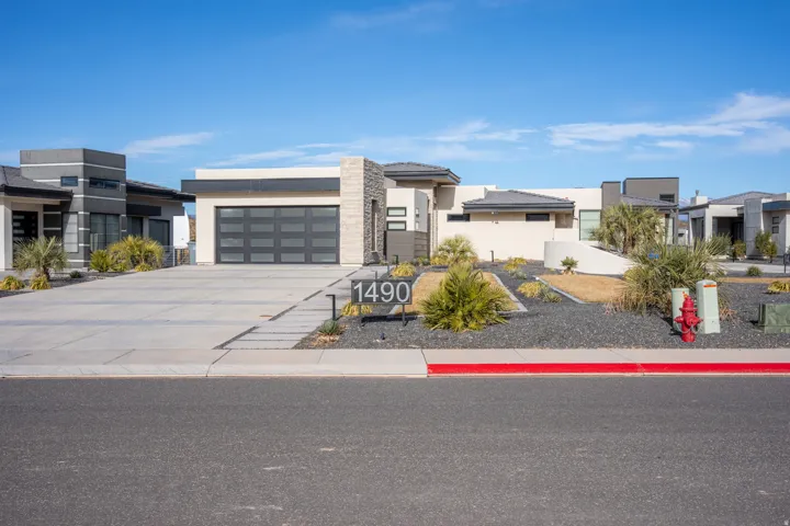 Contemporary exterior with a glass-paneled garage door, stone accent columns, xeriscaped landscaping, a paver driveway, and exterior lighting