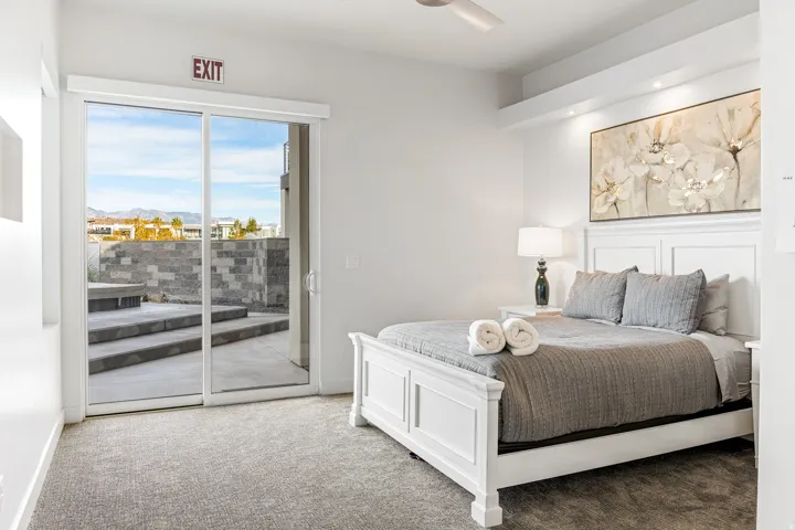 Sliding glass door, textured gray carpeting, integrated ceiling fan, recessed lighting, and a white paneled bed frame