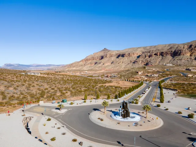 Roundabout with central sculpture, paved roads, arid landscaping, and distant mountain backdrop