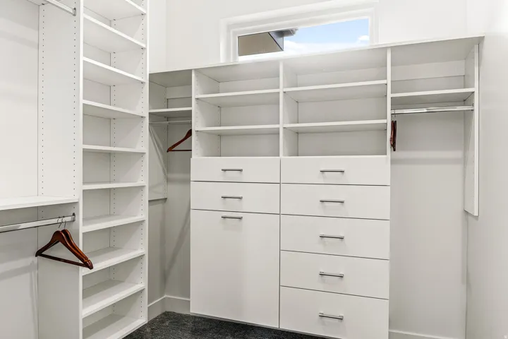 Built-in white cabinetry with chrome hardware, extensive shelving, integrated drawers, and dedicated hanging rods