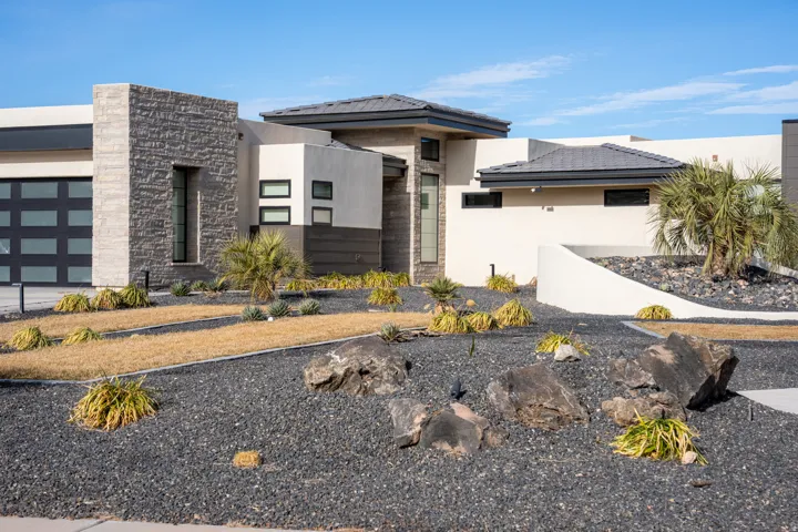 Modern exterior featuring stone veneer accents, stucco siding, a panel garage door, dark gravel landscaping, and established plantings