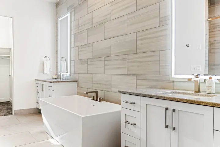 Freestanding soaking tub with a modern faucet, dual vanities with integrated sinks, and illuminated mirrors