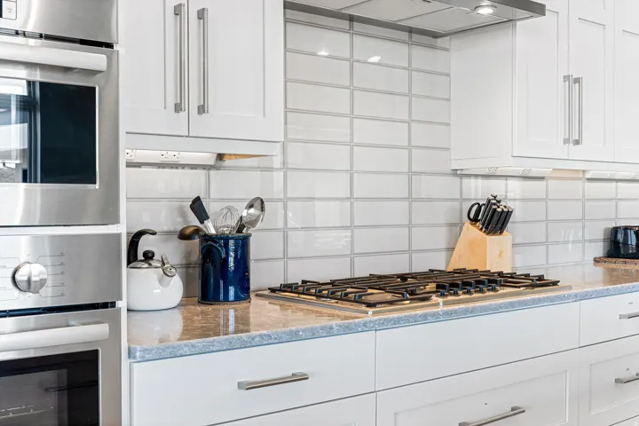 White cabinetry with brushed nickel hardware, built-in stainless steel appliances, a gas range, a light-toned countertop, and a tiled backsplash
