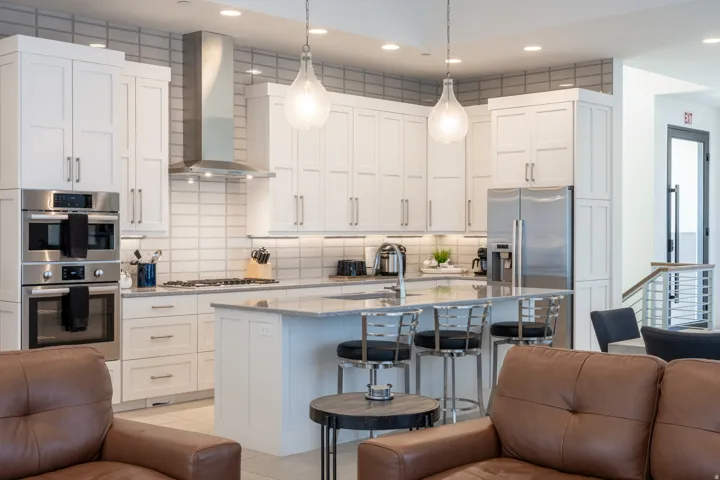 White shaker cabinetry, stainless steel appliances, central island with seating, pendant lighting, and tiled backsplash