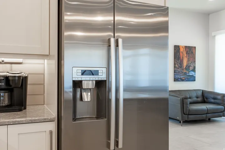 Stainless steel side-by-side refrigerator with integrated ice and water dispenser, light-toned shaker-style cabinetry, and subway tile backsplash