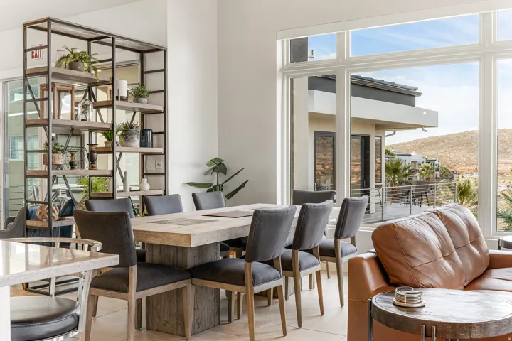 Expansive window wall, open shelving unit, large dining table, spacious balcony, and light-toned flooring