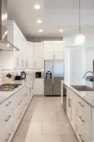 Modern kitchen featuring white shaker cabinetry, stainless steel appliances, a gas cooktop, light-toned tile flooring, and a kitchen island with an undermount sink