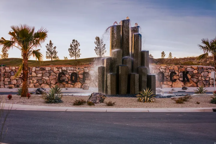 Stone wall with integrated letters, water feature with multiple vertical elements, palm trees, and desert landscaping