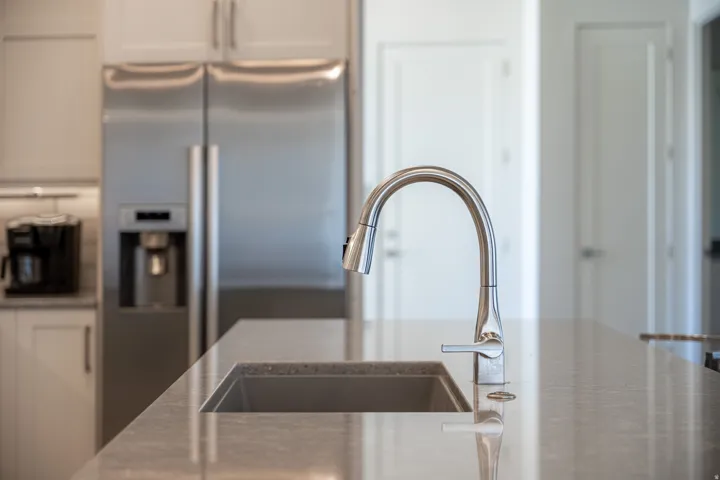 Stainless steel side-by-side refrigerator, under-cabinet lighting, gray cabinetry, undermount sink, and gooseneck faucet