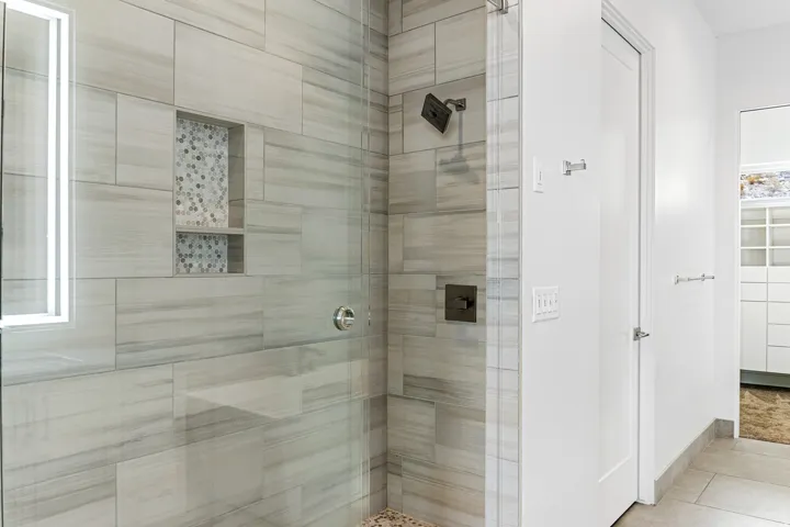 Glass-enclosed shower with gray-toned tile walls, built-in shower bench, and recessed tiled niche