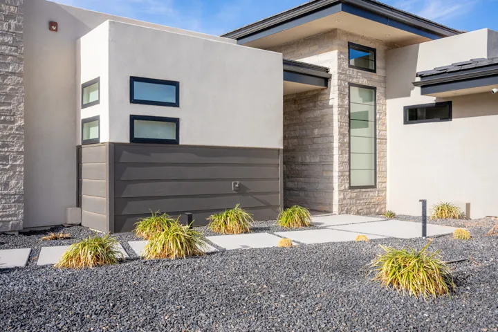 Modern exterior featuring a stacked stone facade, stucco finishes, dark horizontal siding, square concrete pavers, and dark gravel landscaping