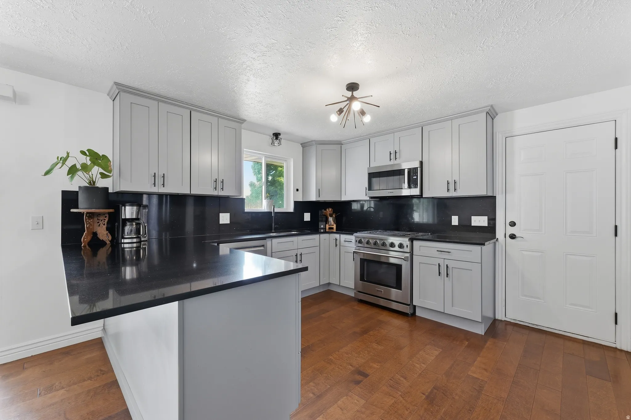 Modern kitchen featuring light gray cabinetry, dark countertops, stainless steel appliances, and wood-finish flooring