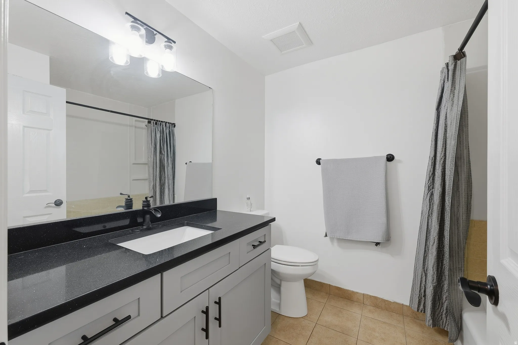 White vanity with a dark countertop, undermount sink, and black fixtures