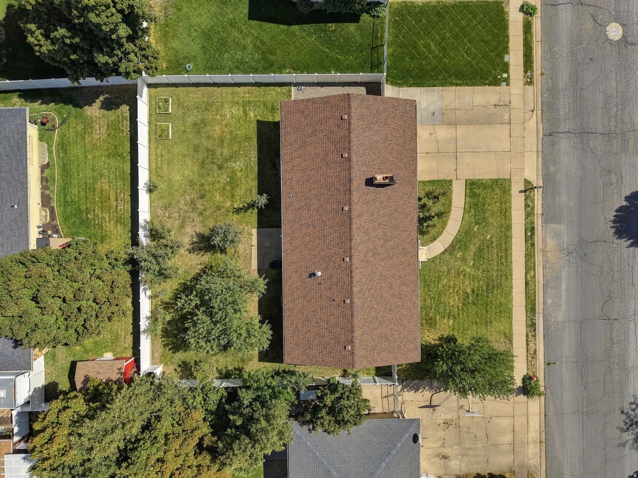 Gable roof with a visible chimney, concrete driveway, front lawn with a curved walkway, rear lawn with planted trees, and a privacy fence enclosing the backyard