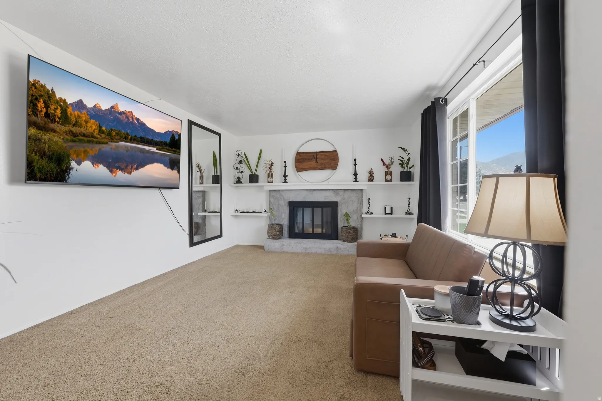 Living area featuring a textured carpet, a fireplace with a stone surround, an expansive window, and a wall-mounted television