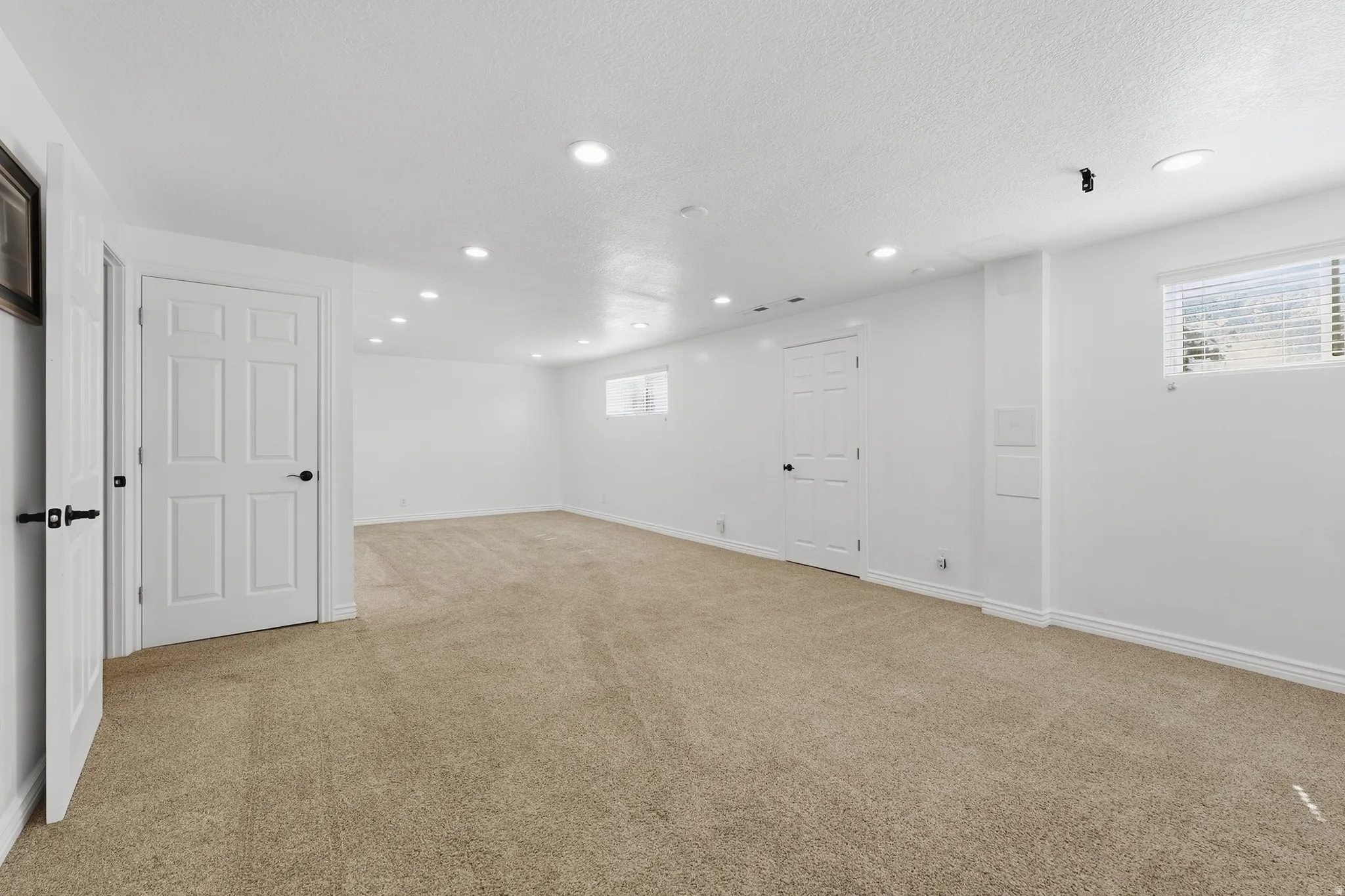 Spacious room with recessed lighting, light-colored carpeting, multiple doors, and a window with blinds