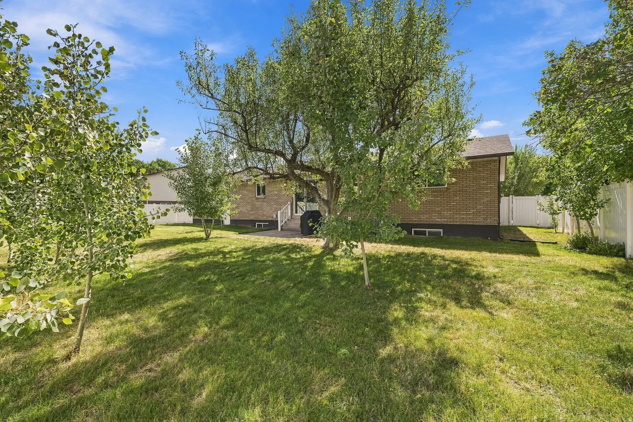 Expansive rear yard featuring green lawn, mature trees, and a brick exterior