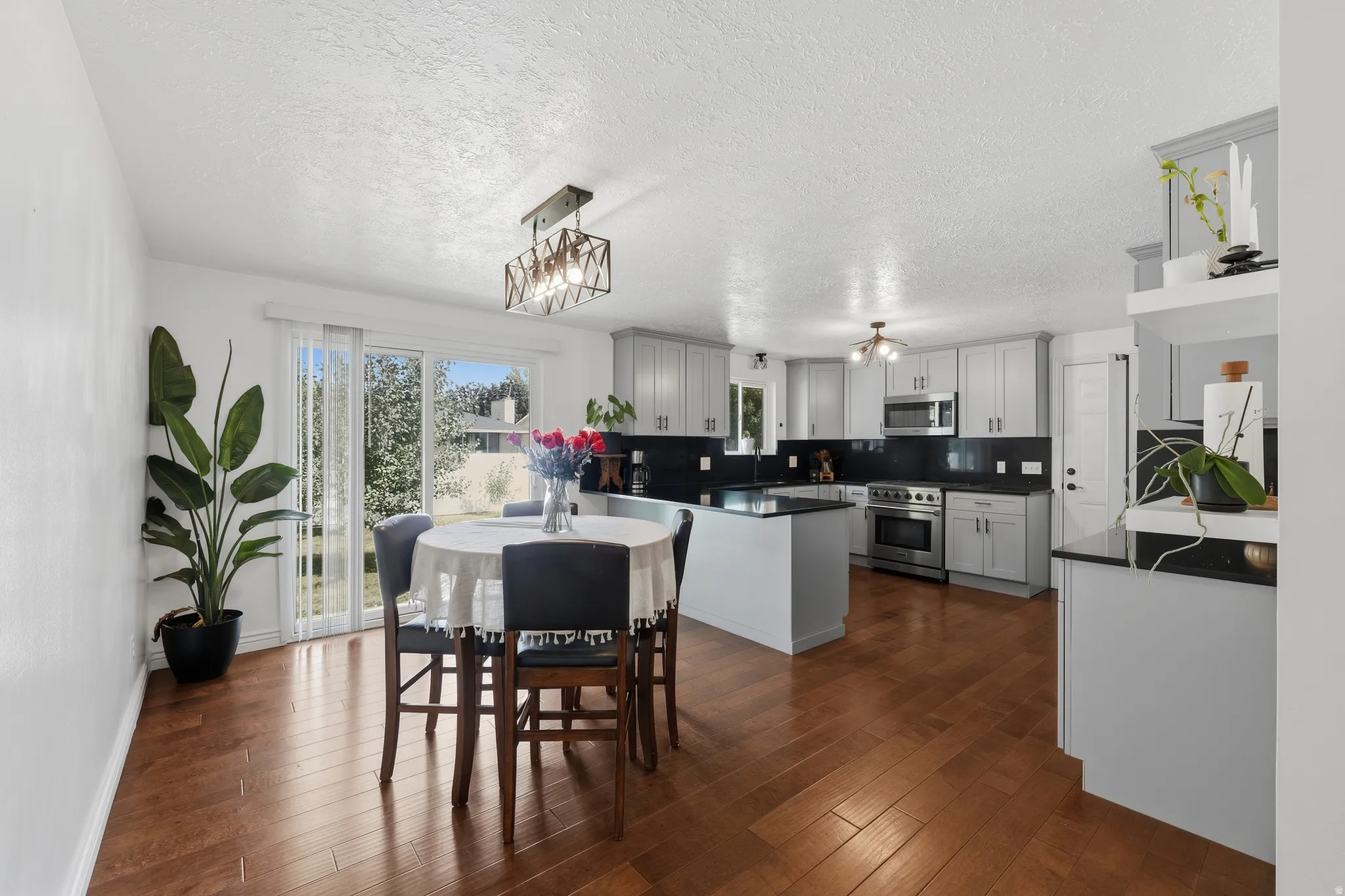 Wood-finish flooring throughout, sliding glass door with backyard access, light gray cabinetry, dark countertops, and stainless steel appliances