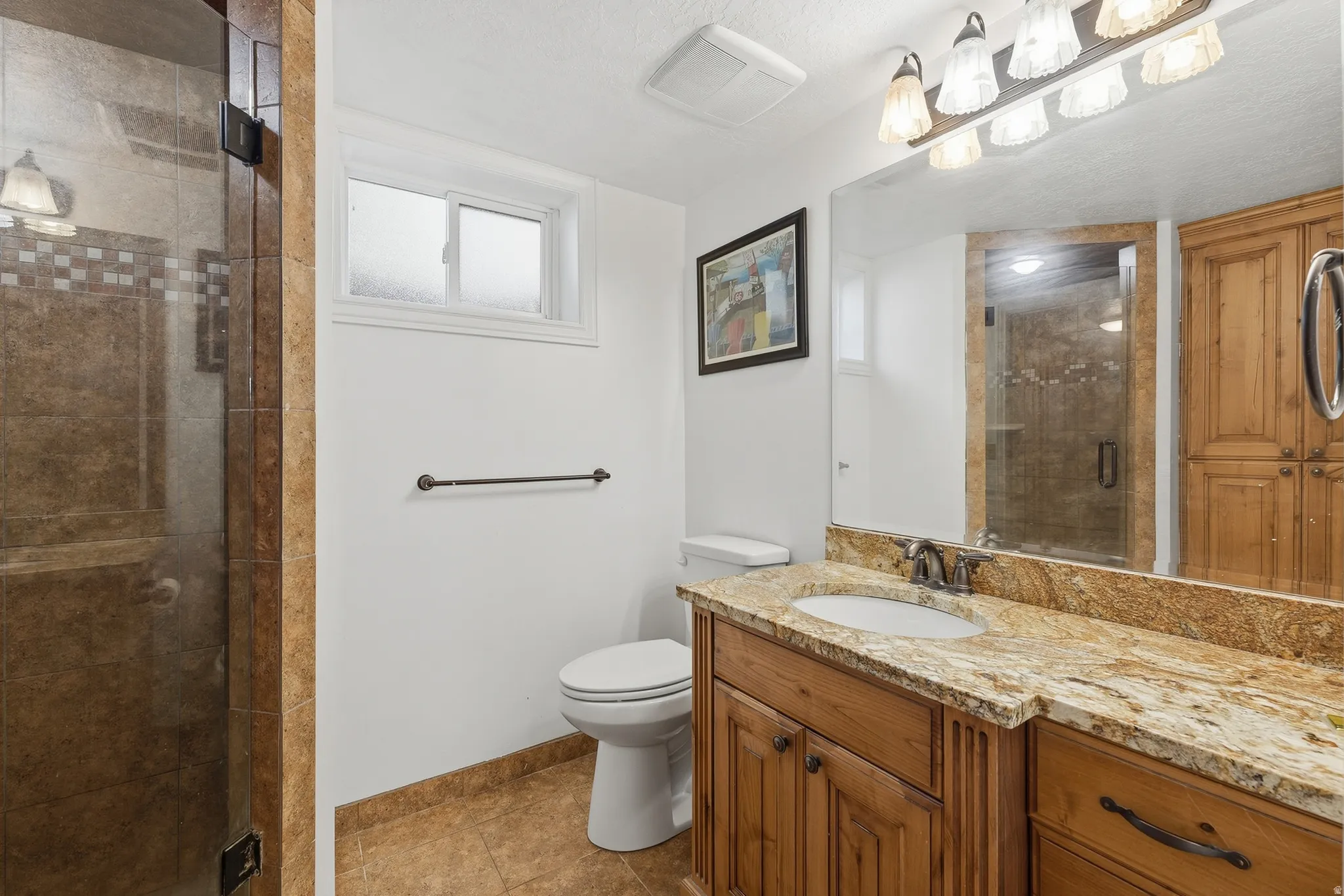Tiled walk-in shower with glass enclosure, wood-finish vanity with an integrated sink, granite countertop, and tile flooring