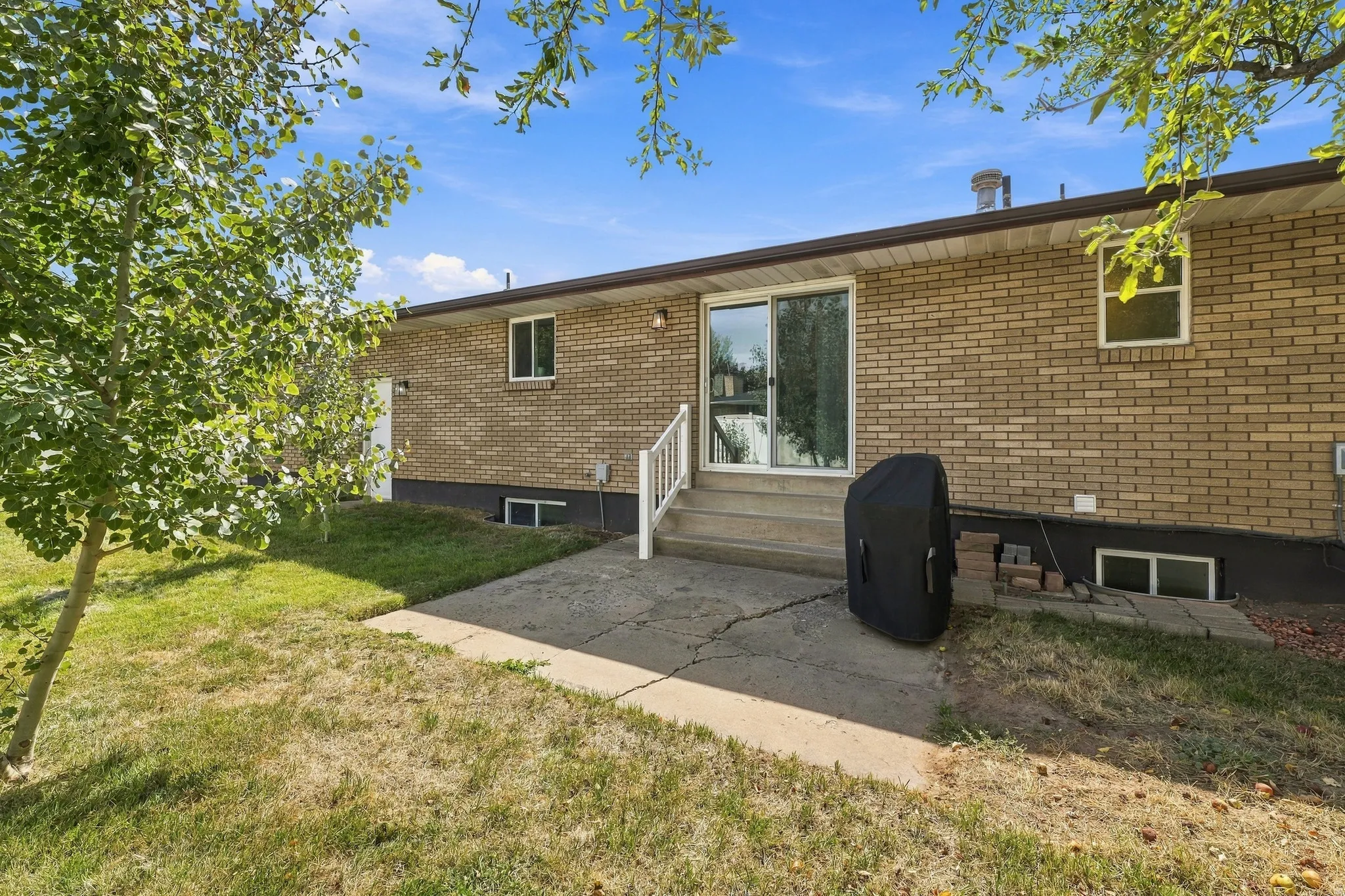 Brick exterior with a concrete patio, sliding glass door, and white handrails