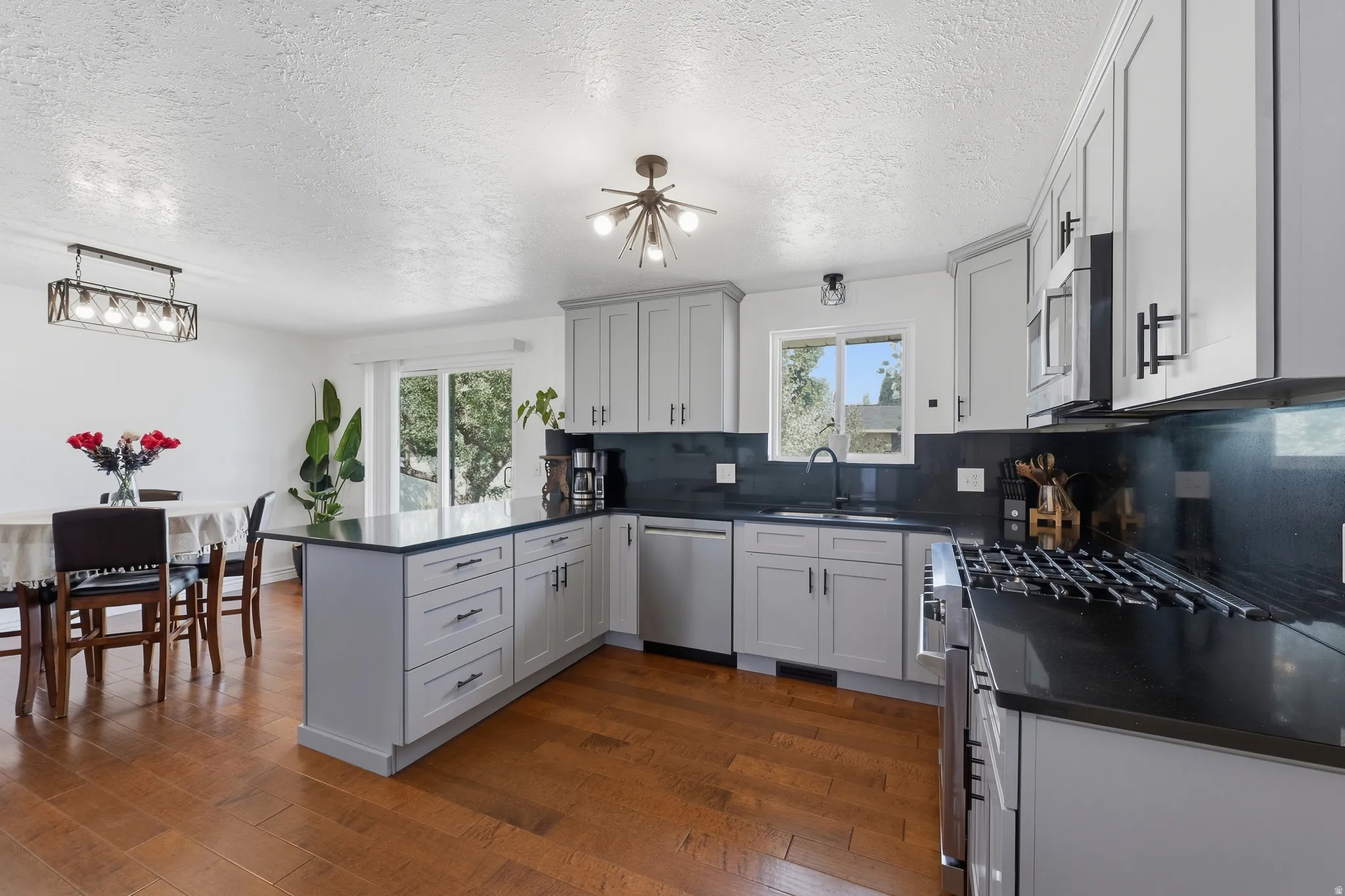 Kitchen featuring wood-finish flooring, light gray cabinetry with dark hardware, dark countertops, stainless steel appliances, and a central island