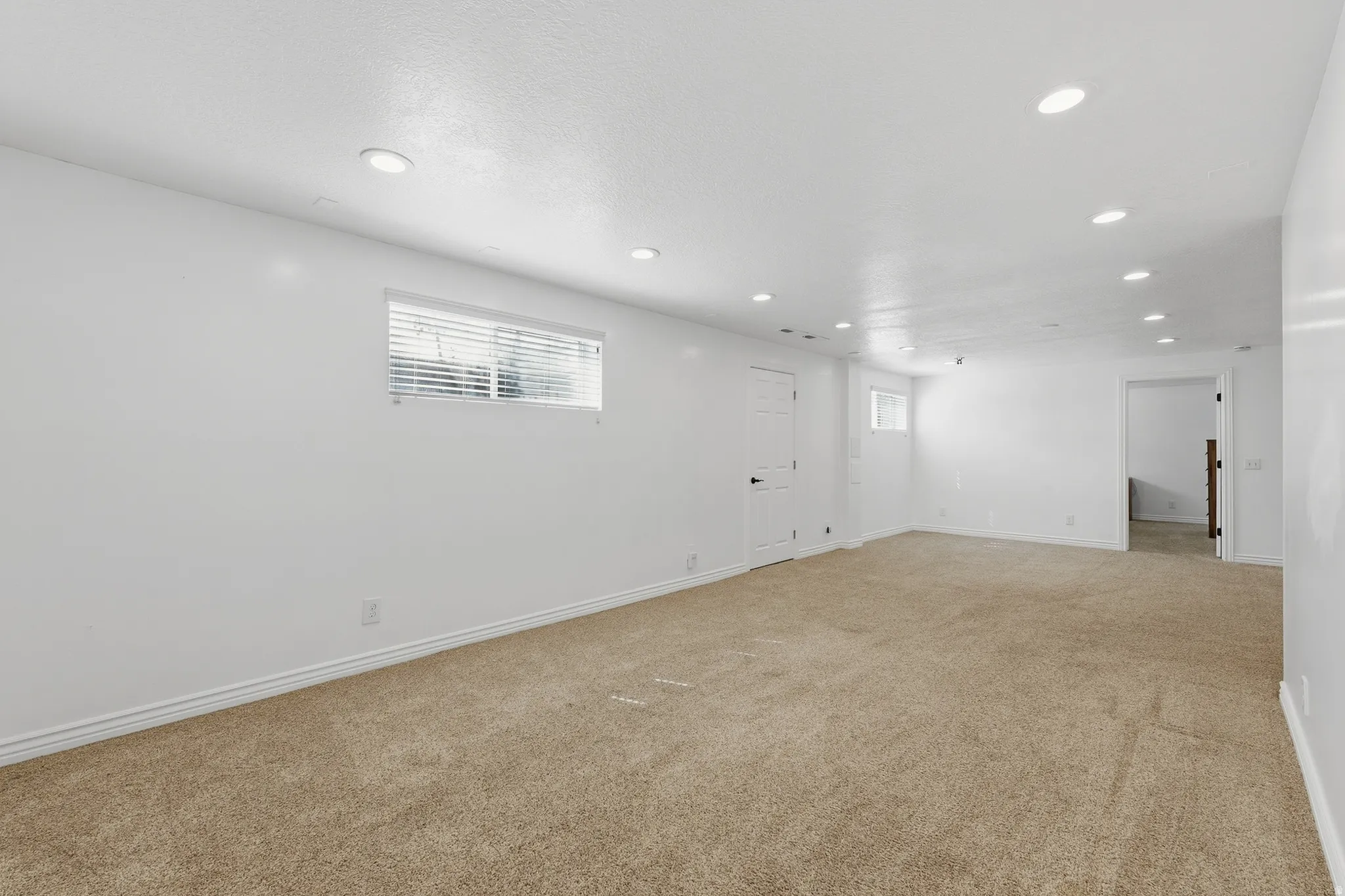Spacious room with recessed lighting, light-toned carpeting, a window with blinds, and white walls