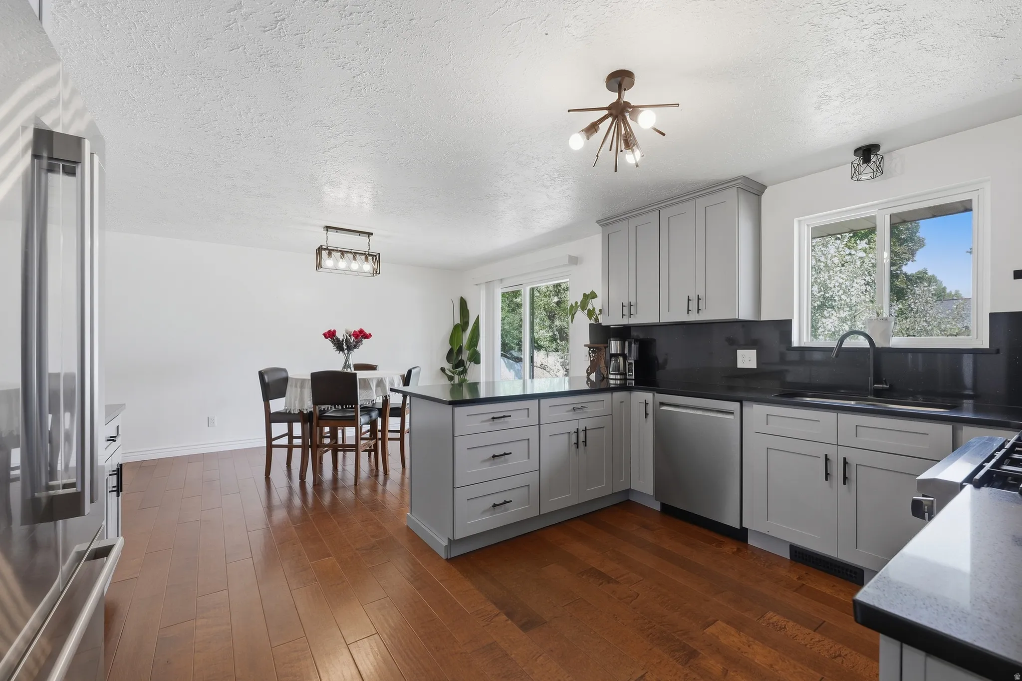 Updated kitchen with light gray cabinetry, dark countertops, stainless steel appliances, and wood-finish flooring