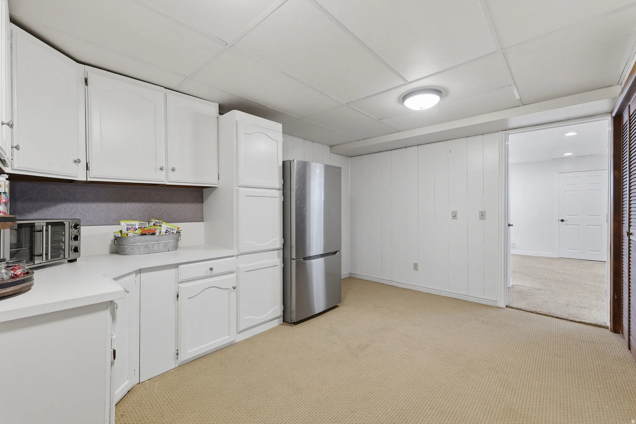 White cabinetry with silver-tone hardware, light countertops, and a stainless steel refrigerator