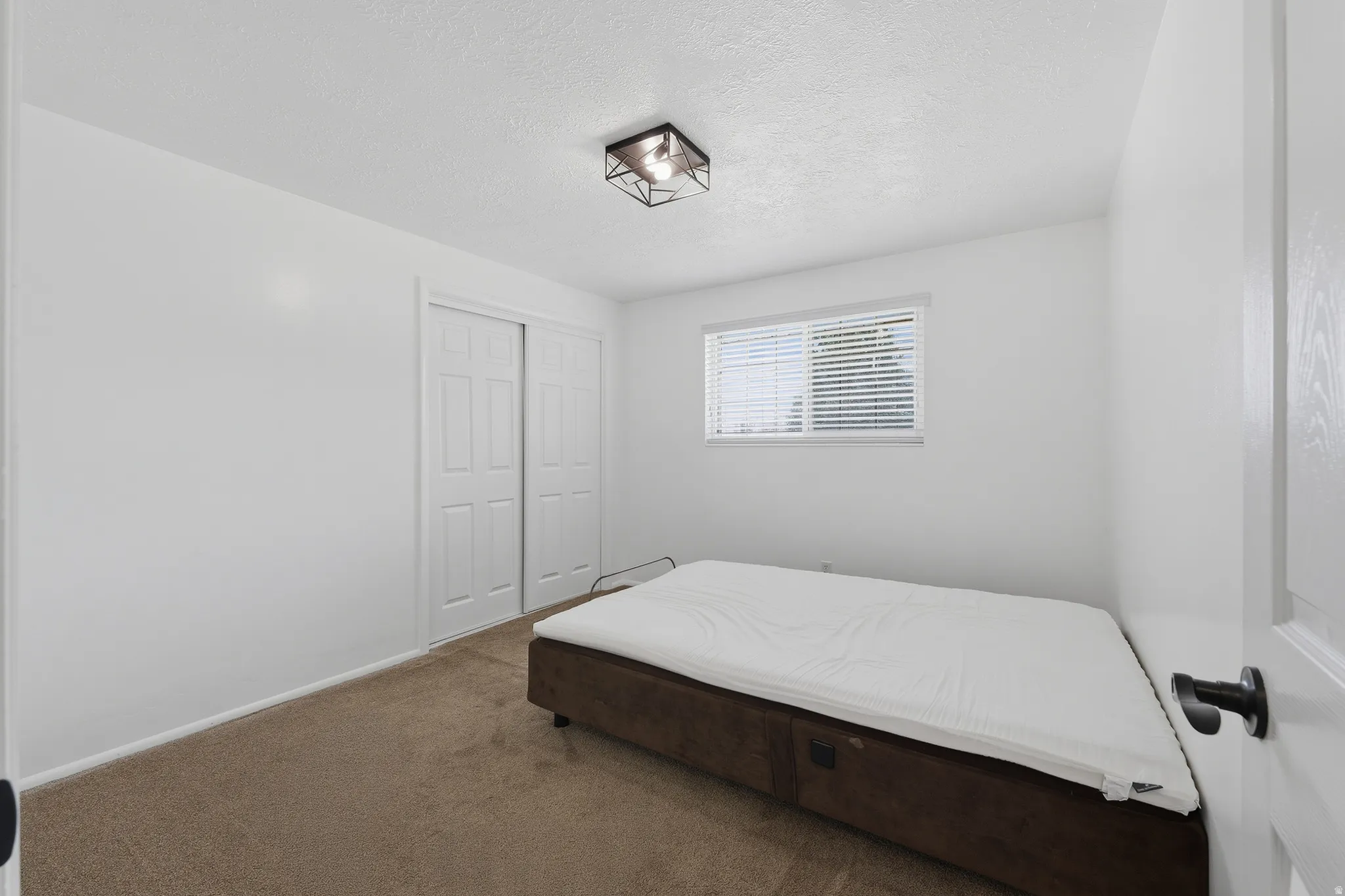 Neutral wall colors, carpet flooring, a window with horizontal blinds, and a built-in closet with bifold doors