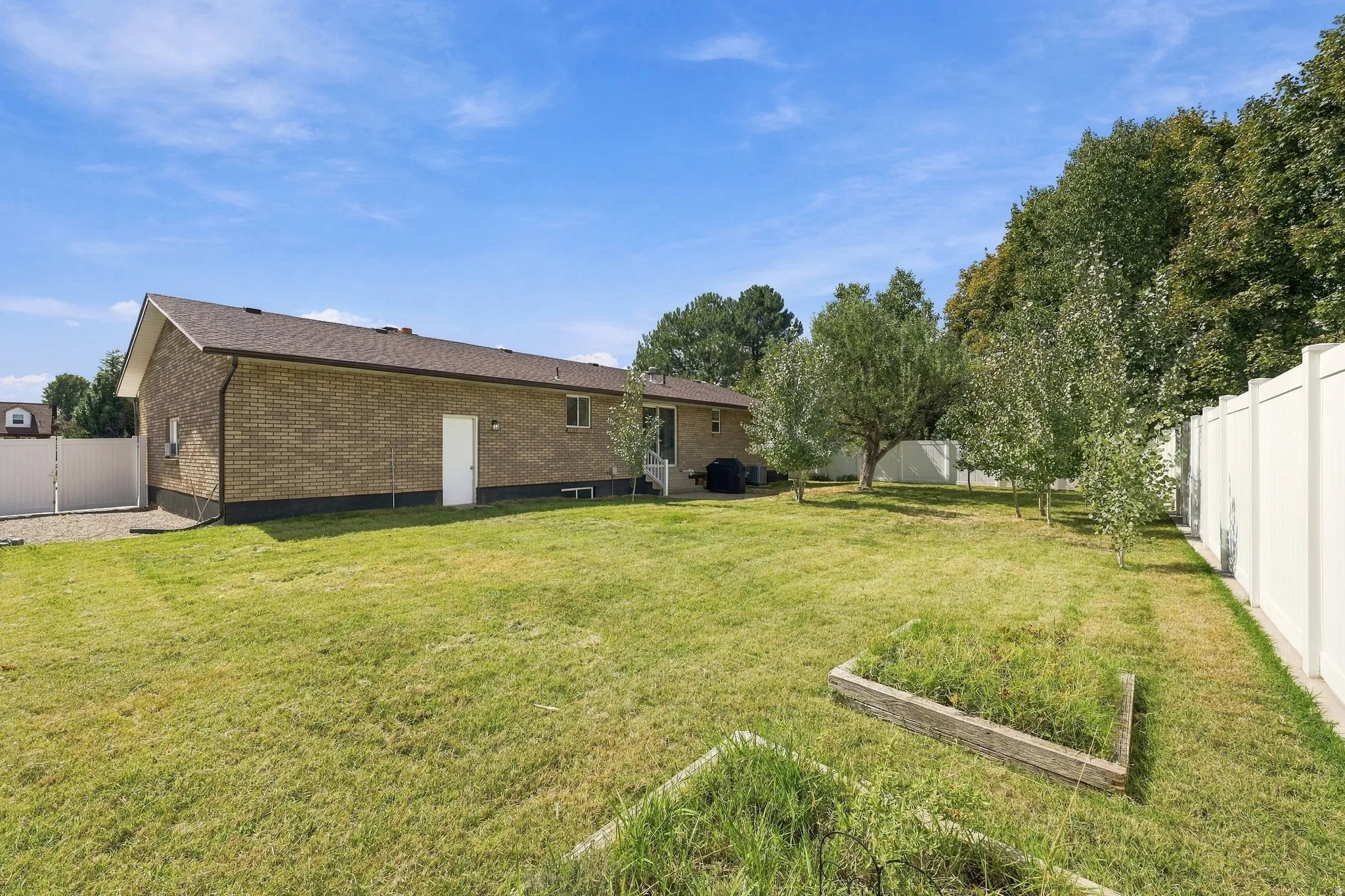 Expansive backyard with a manicured lawn, established trees, and a durable vinyl privacy fence