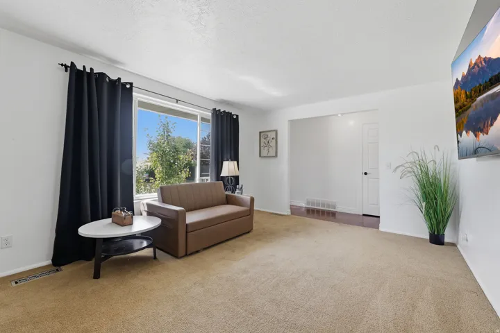 Bright living area featuring a large window, light-toned carpeting, and a white interior door