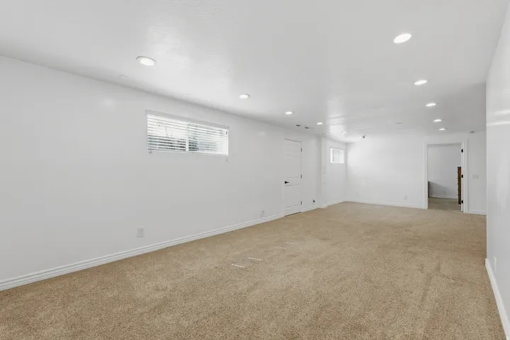 Spacious room with recessed lighting, light-toned carpeting, a window with blinds, and white walls