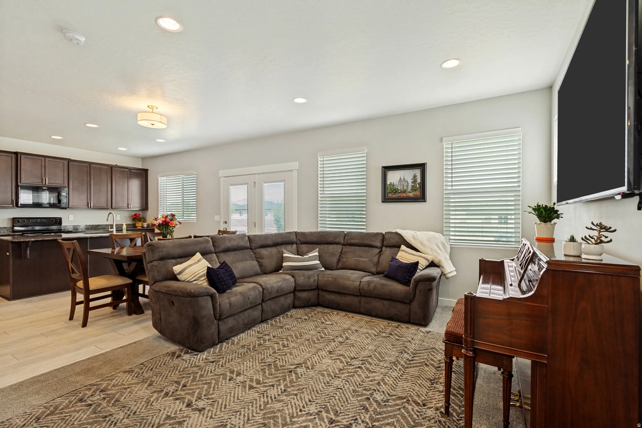 Open concept living area featuring recessed lighting, a kitchen with dark wood-finish cabinetry, light wood-finish flooring, and French doors