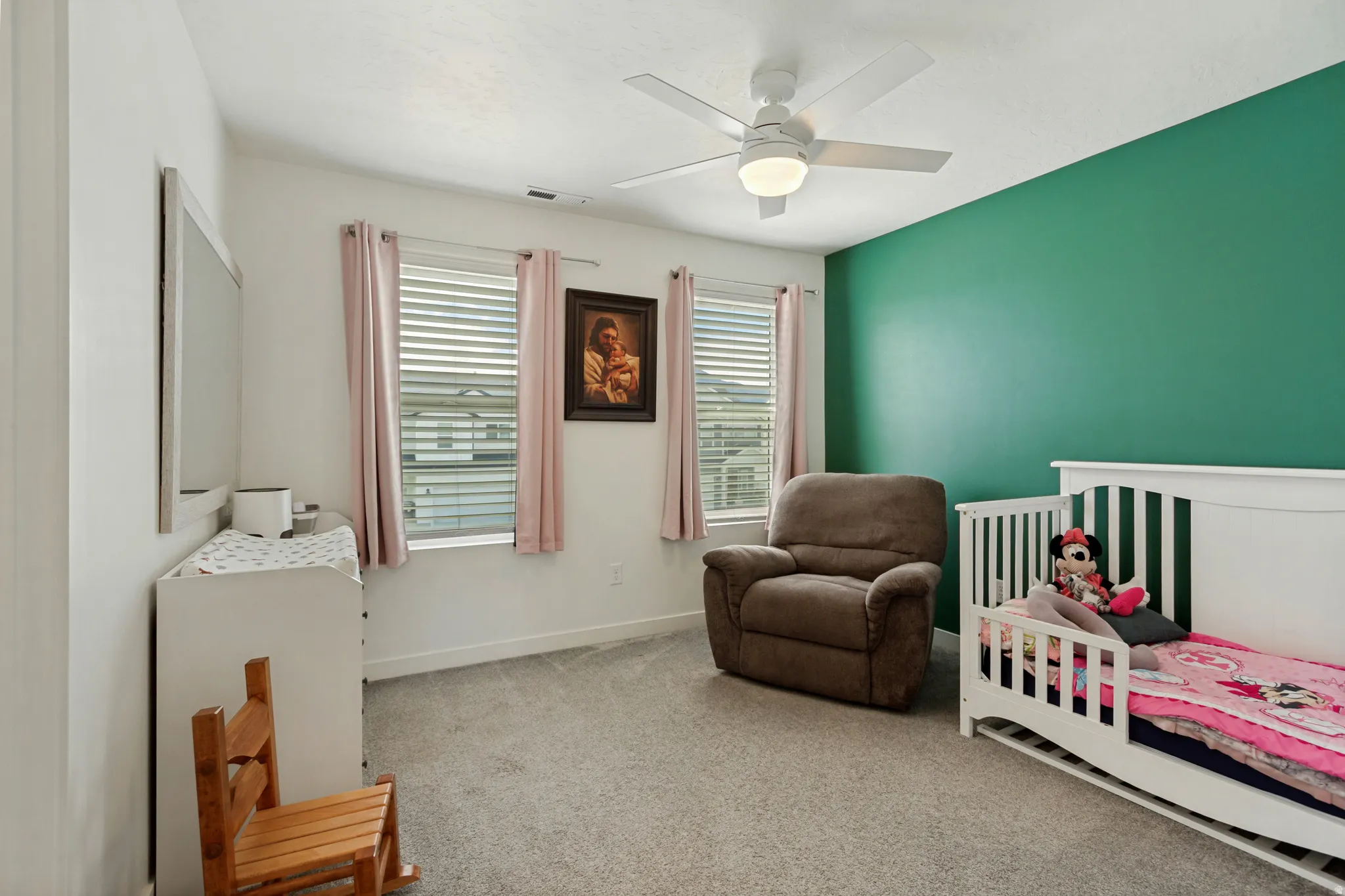 Carpeted interior space with a ceiling fan, dual windows, and an accent wall